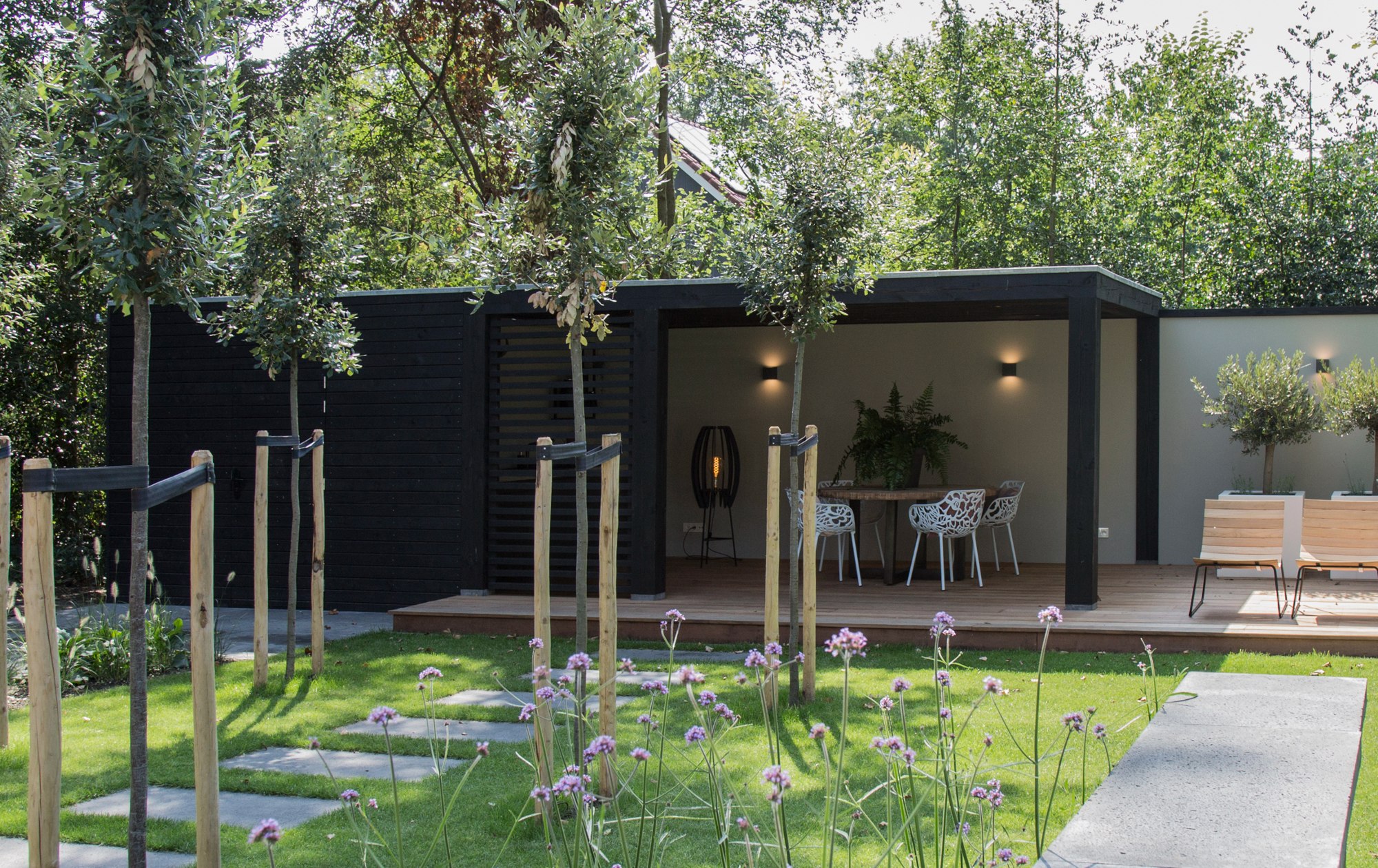 Tuinkamer van hout in het zwart met een vlonder en betonlook achterwand